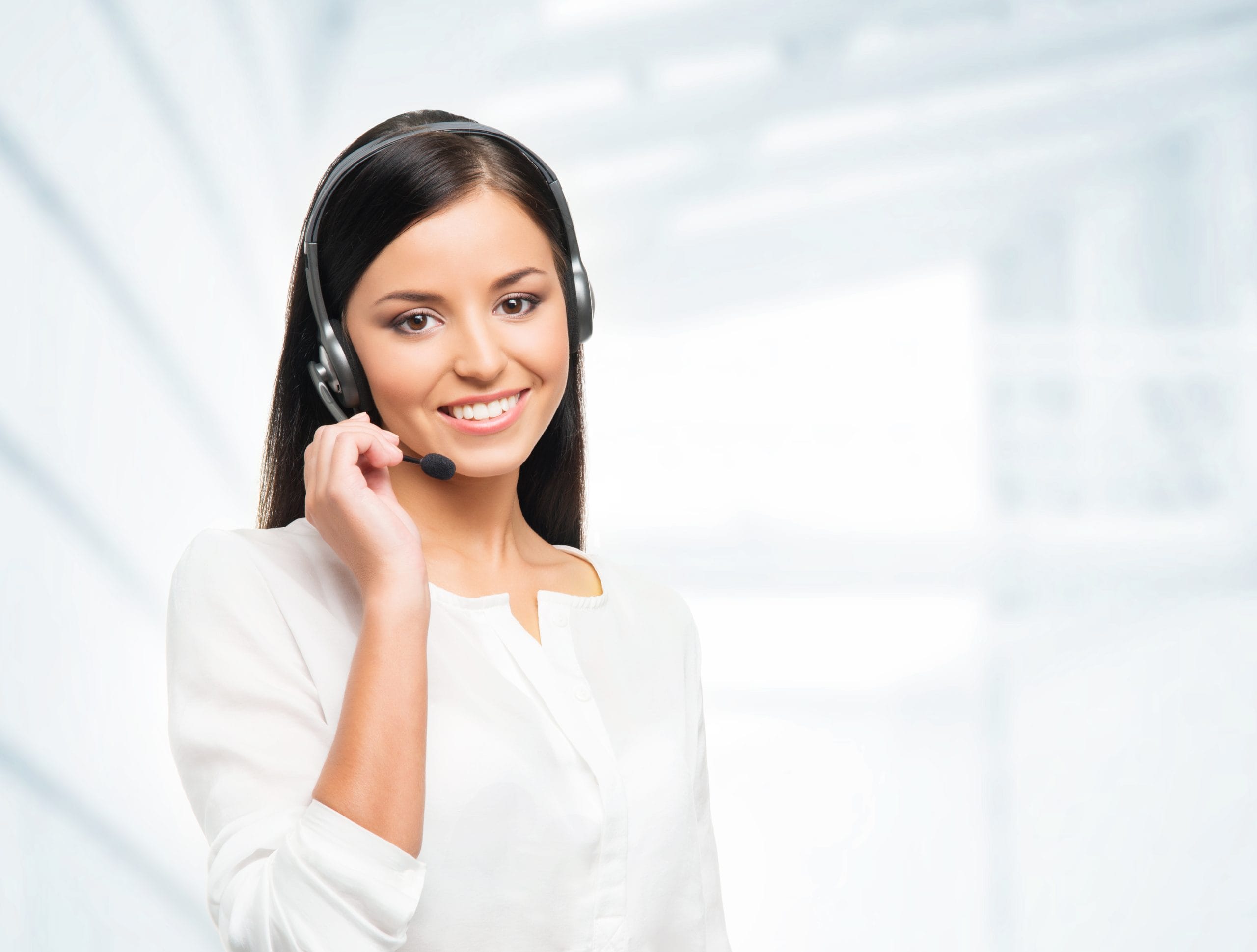 A smiling female customer support representative with long black hair, wearing a headset and a white blazer