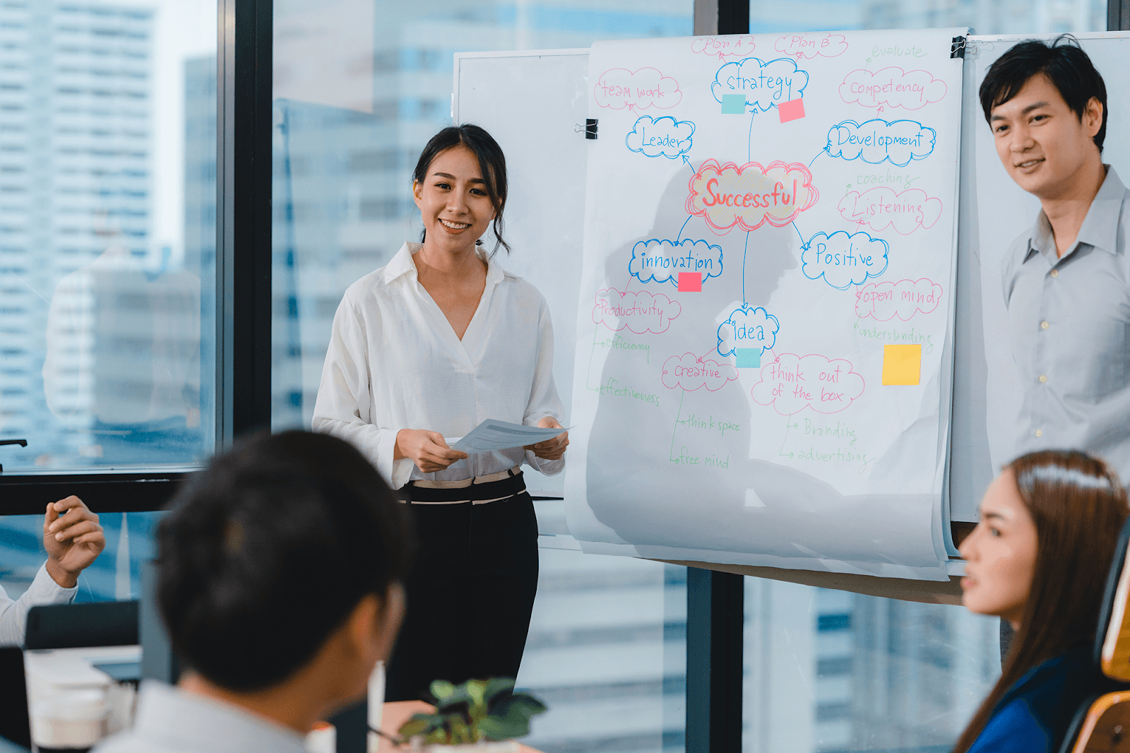 A woman presenting on a whiteboard to her colleagues in a modern office.