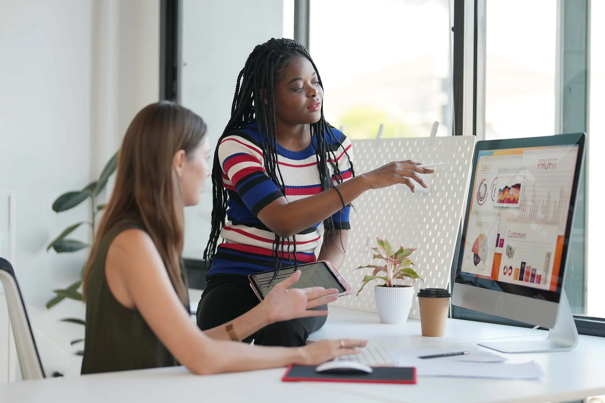 Two women are seated at a table, reviewing the audience’s sentiment analysis for their retail brand on the computer screen.