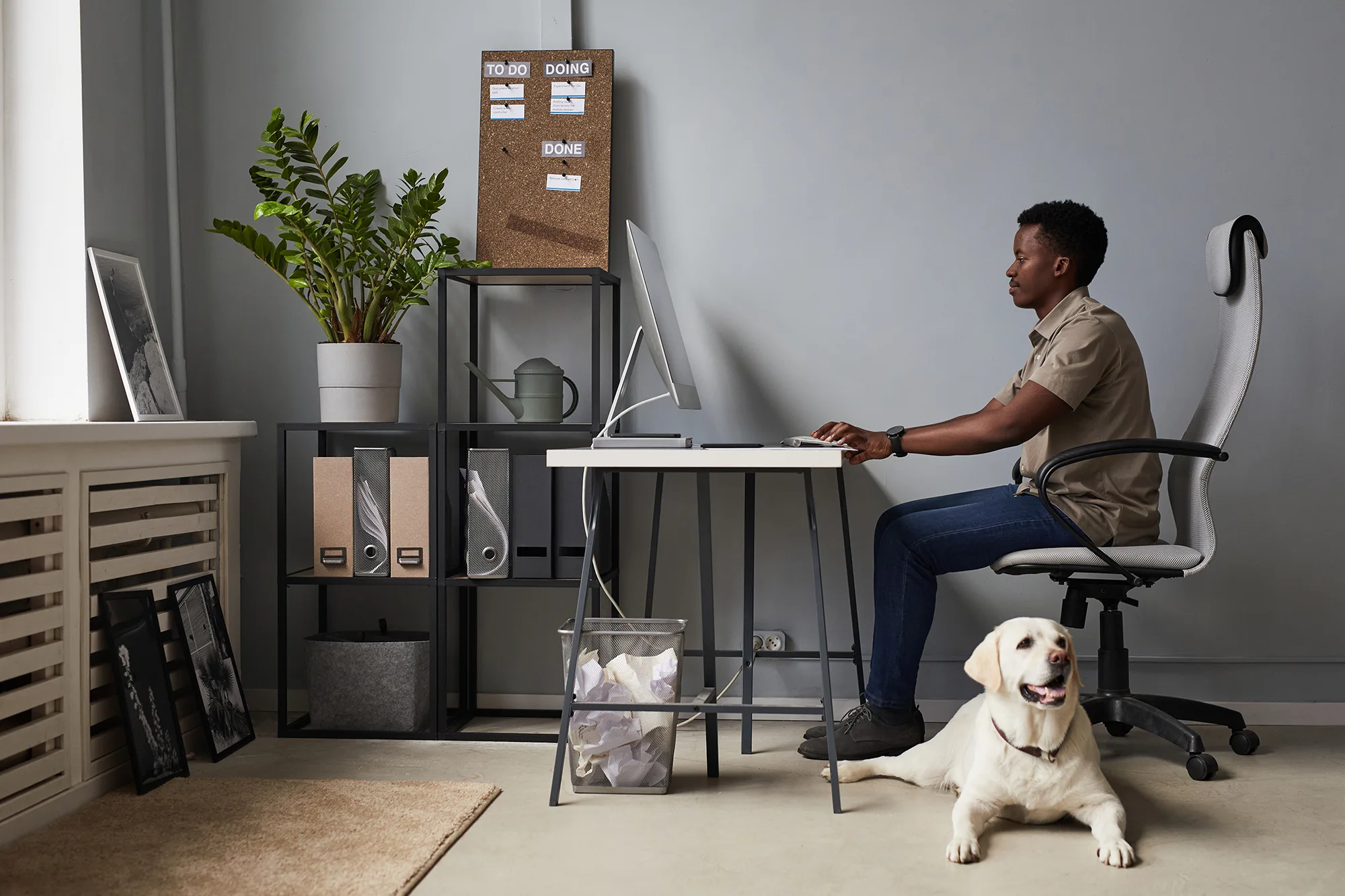 A person working remotely at their own comfortable workstation. A white Labrador Retriever is resting on the floor.