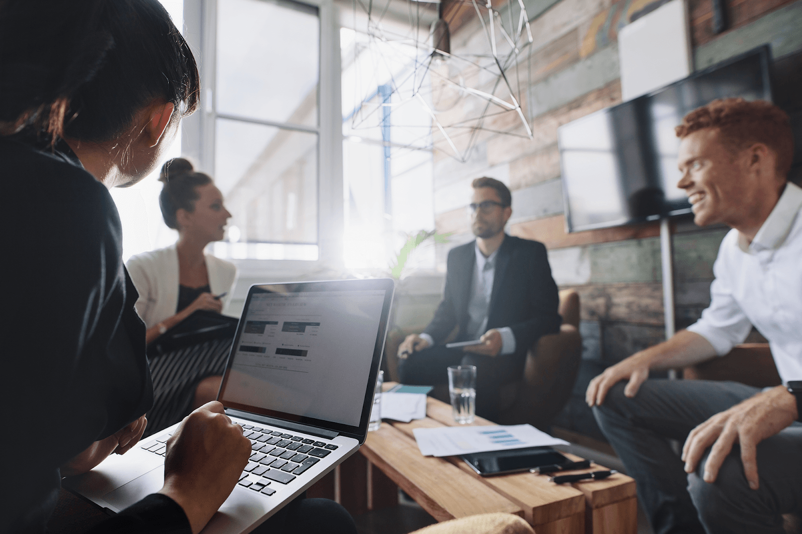 A group of professionals in a modern office setting are collaborating around a wooden table.