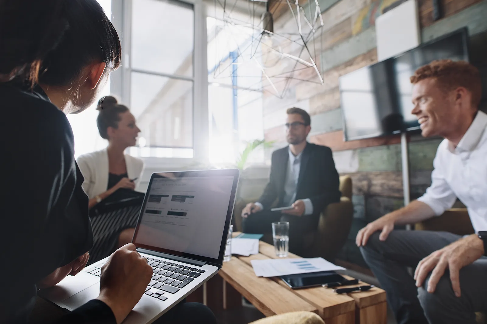 A group of professionals in a modern office setting are collaborating around a wooden table.