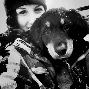A selfie of a woman wearing a winter hat and a checked jacket, cuddling a dog