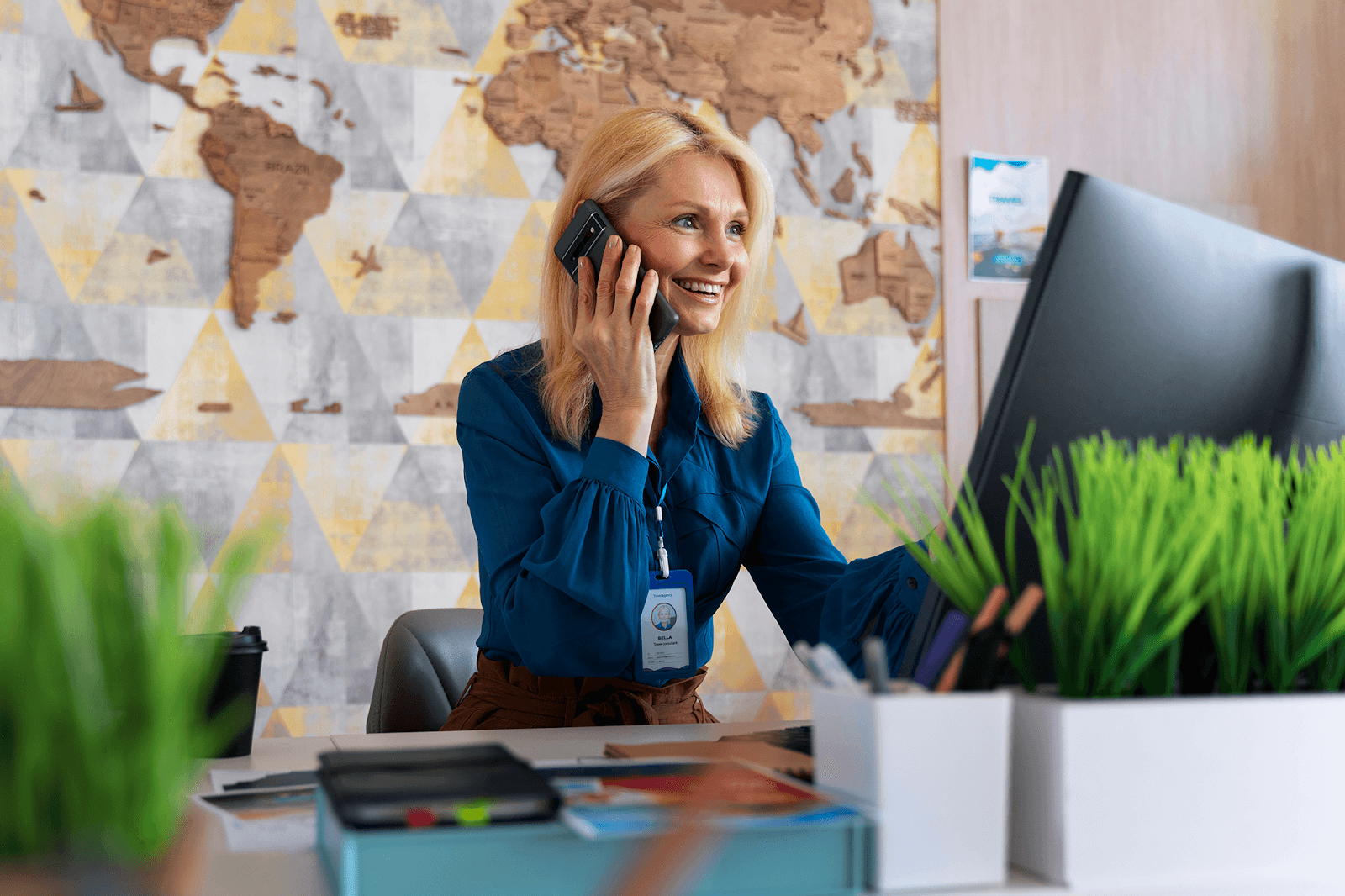 A blonde woman wearing a blue blouse smiles as she talks on the phone.