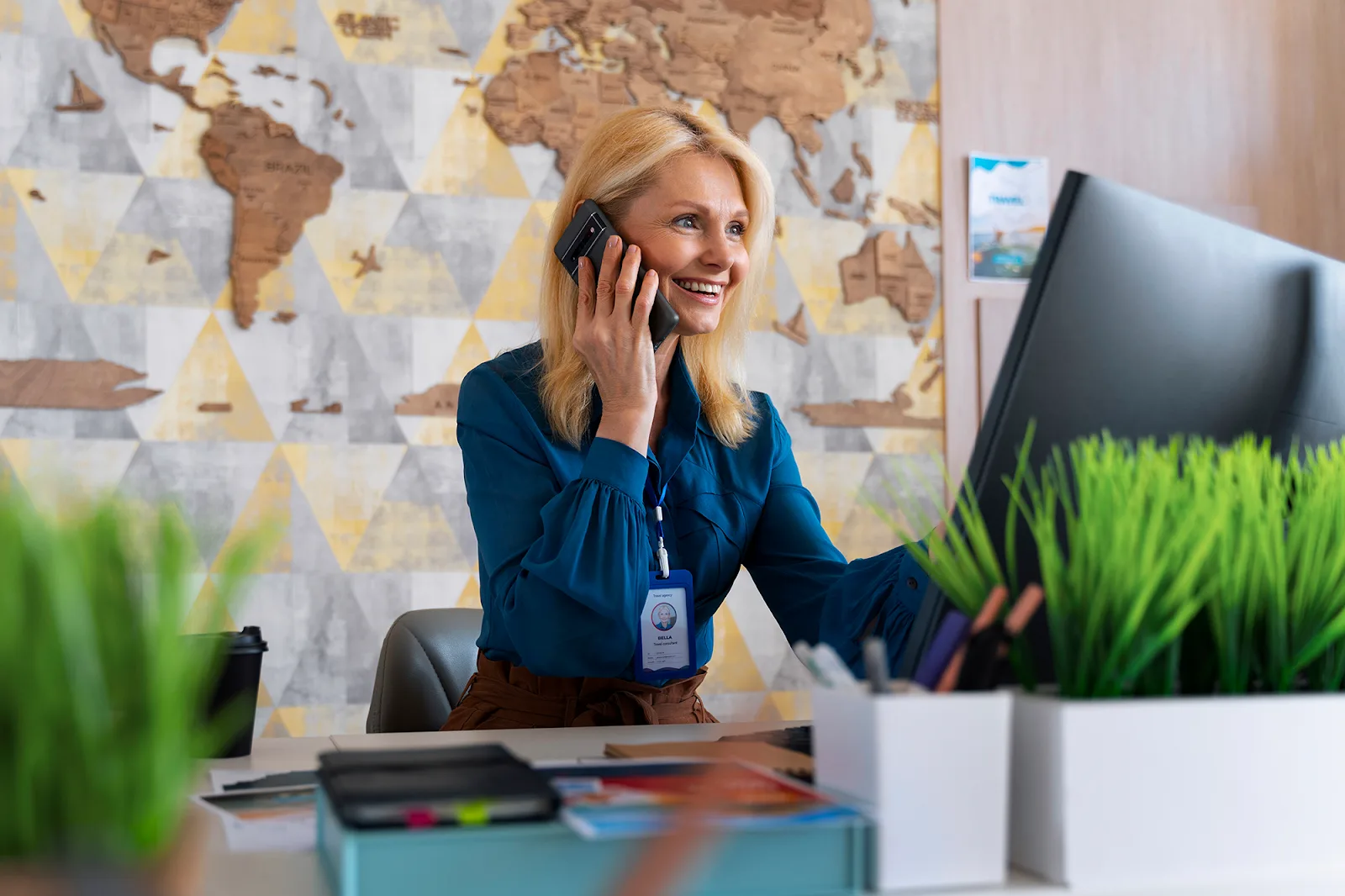 A blonde woman wearing a blue blouse smiles as she talks on the phone.