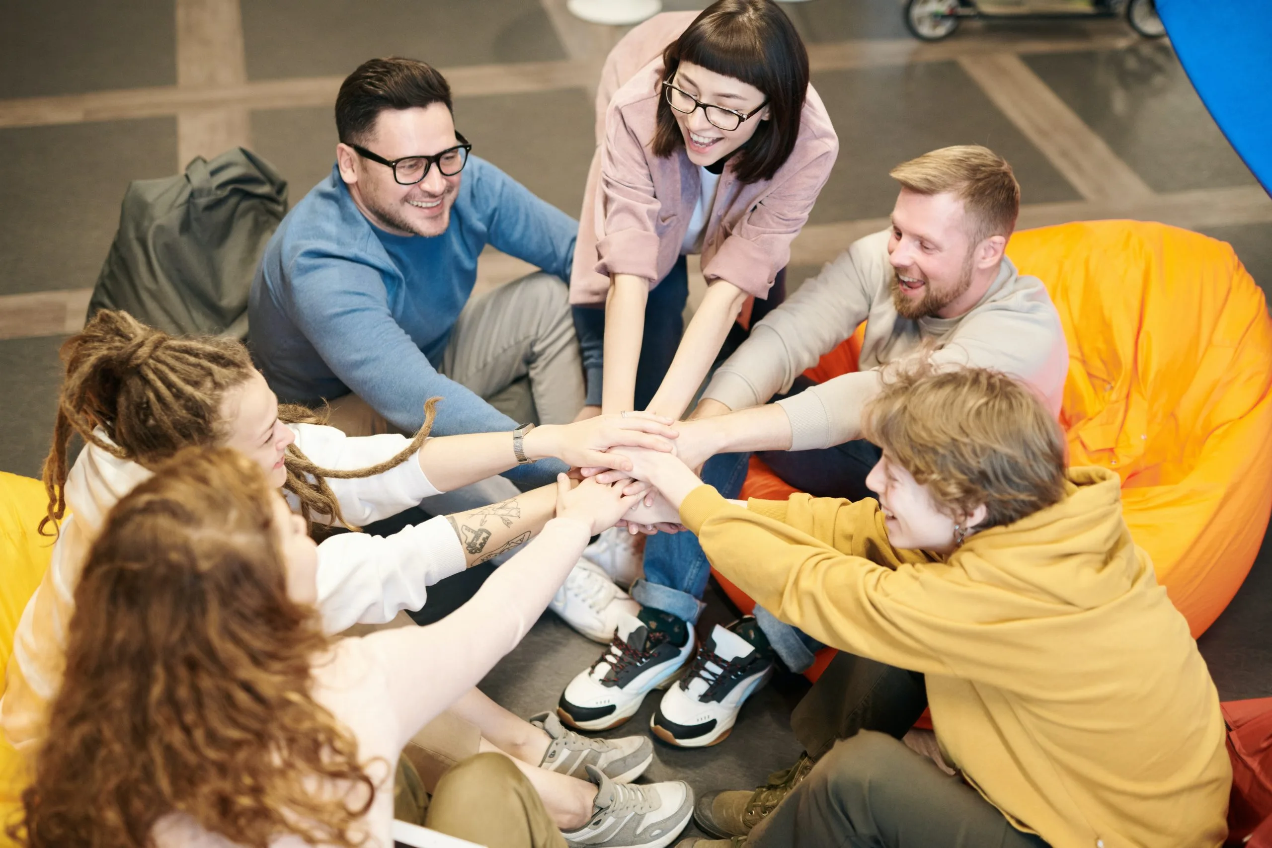 A group of young adults are sitting in a circle with their hands stacked together
