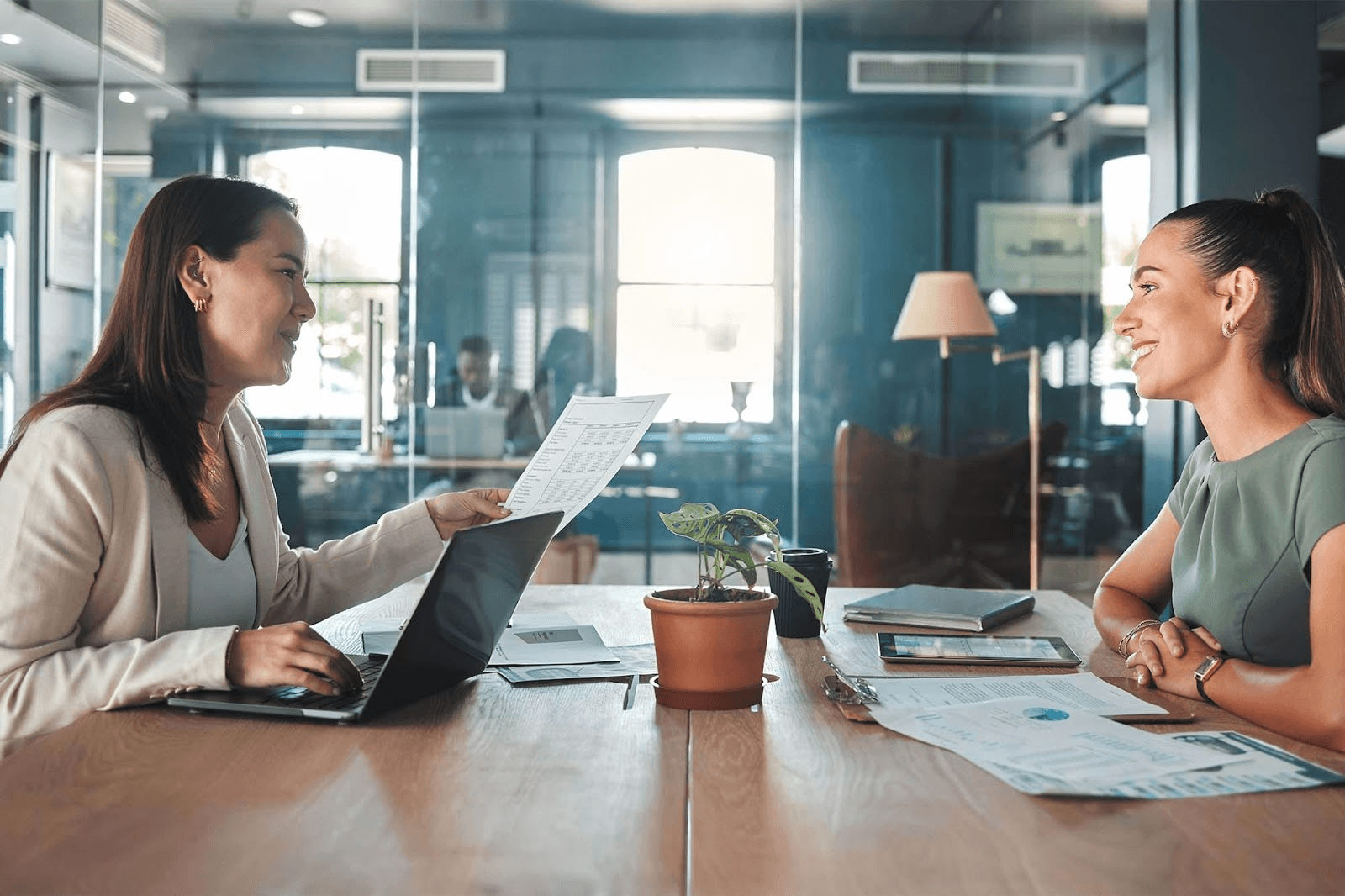 Two women meeting in an office with documents and a laptop.