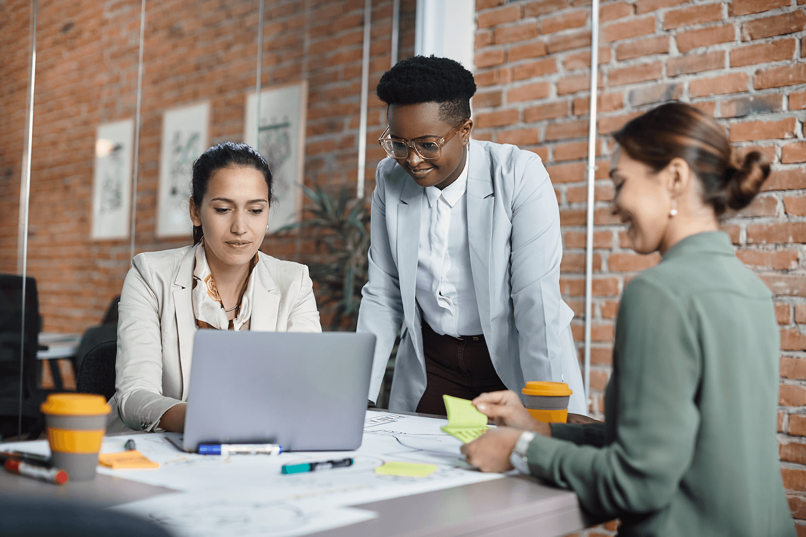 A team of women collaborating on a project, planning with a laptop and reviewing documents in a modern office setting.
