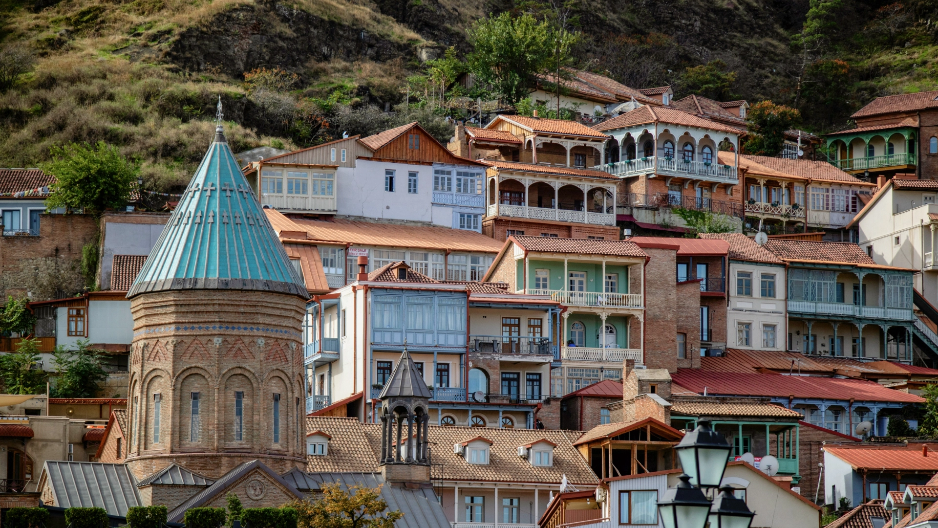 Georgia, featuring traditional houses clustered on a hillside and a prominent church with a turquoise dome. 