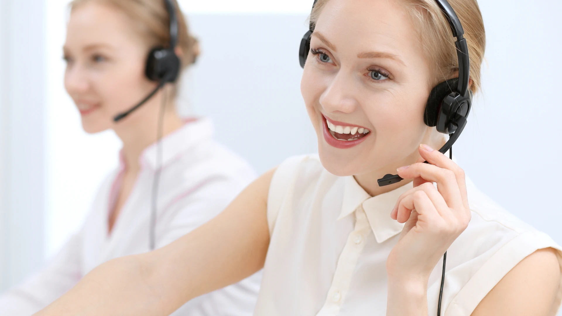 A smiling woman wearing a headset, providing customer support. Another agent is visible in the background.