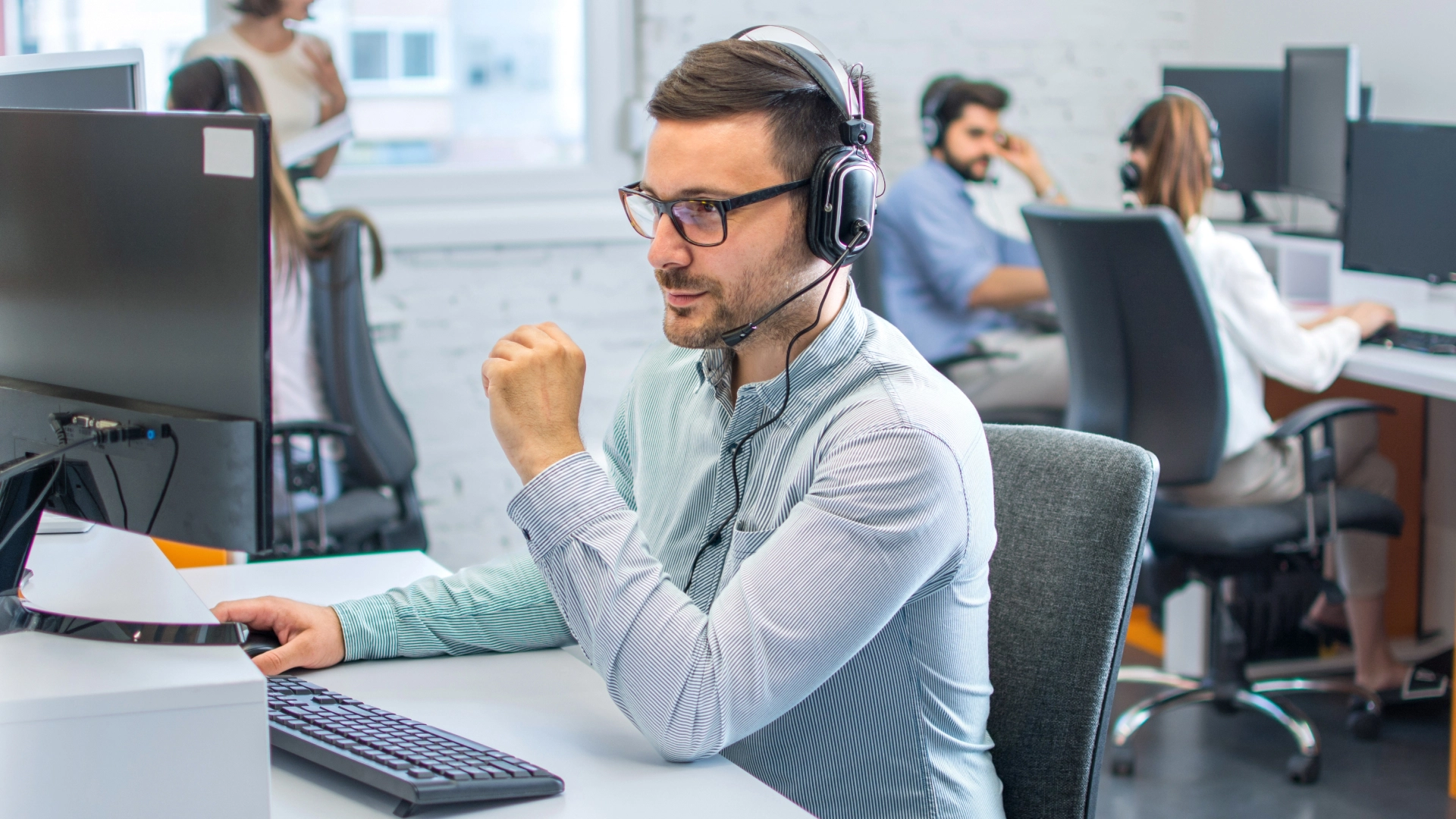 Customer support representative with glasses and headset, working attentively at a computer.