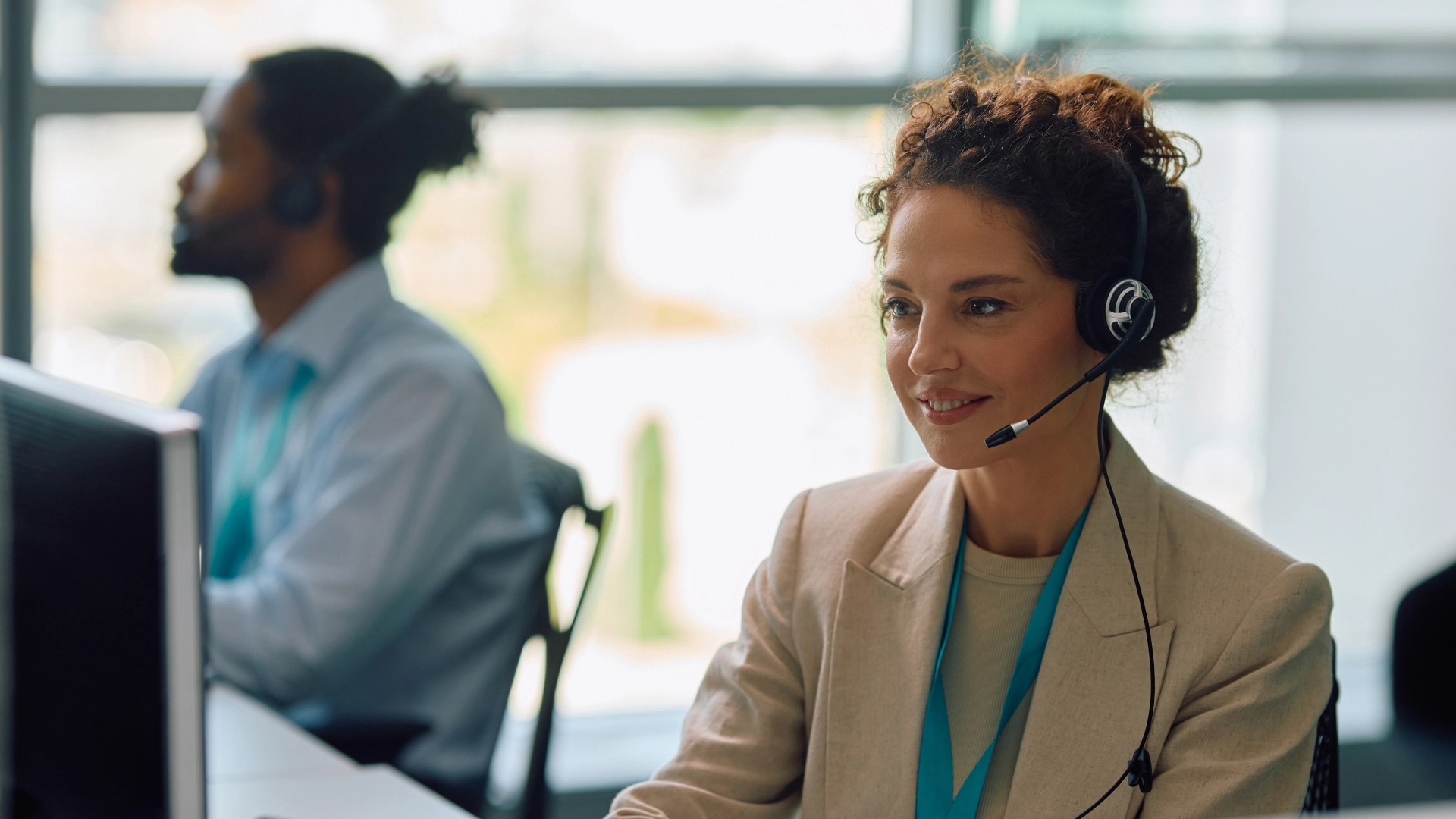 A professional customer service representative with a headset working at a computer in a modern office.